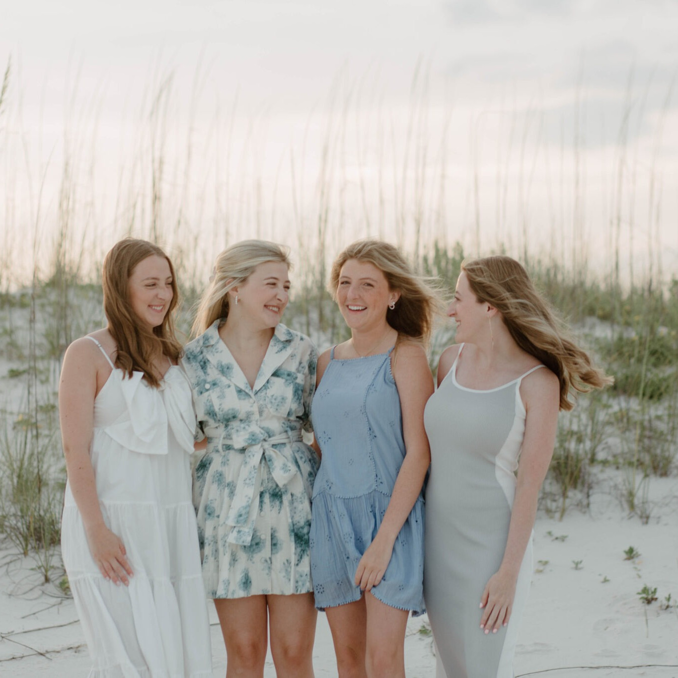 Four women in coordinating floral and blue dresses standing in the dunes at Navarre Beach.