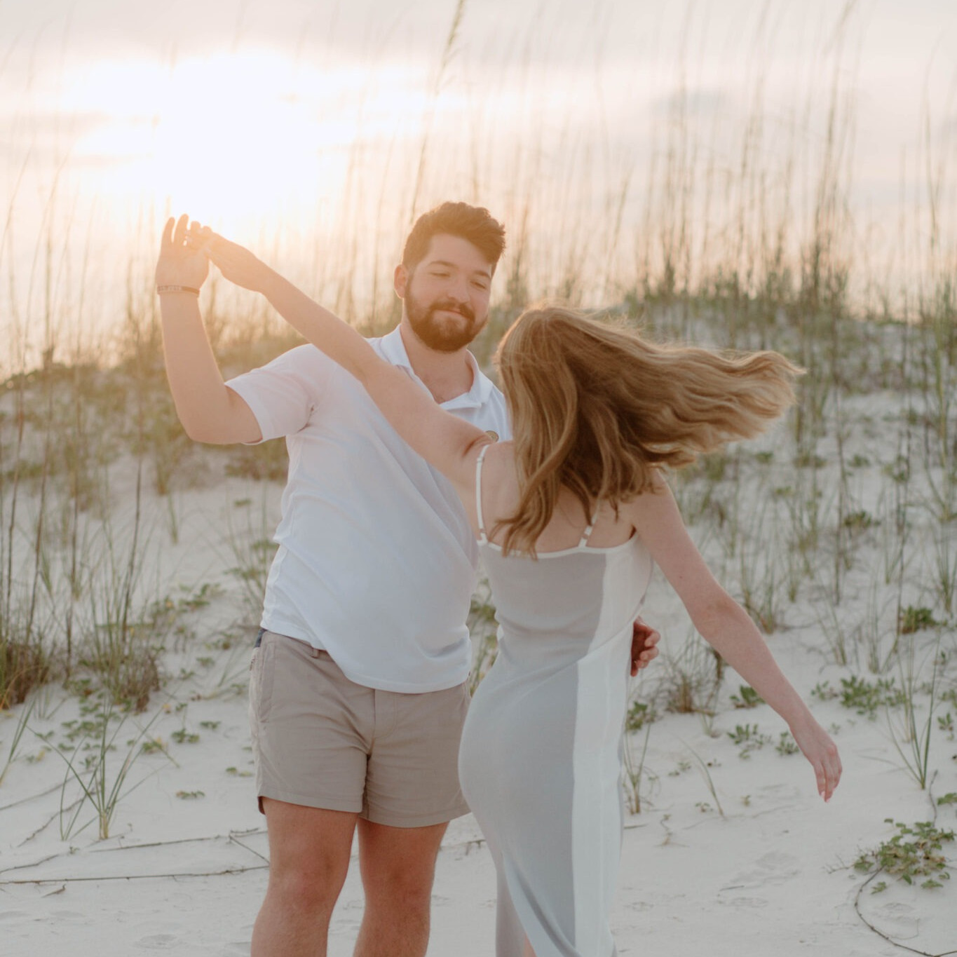 Happy couple laughing and spinning together on the sand during a sunset photography session.