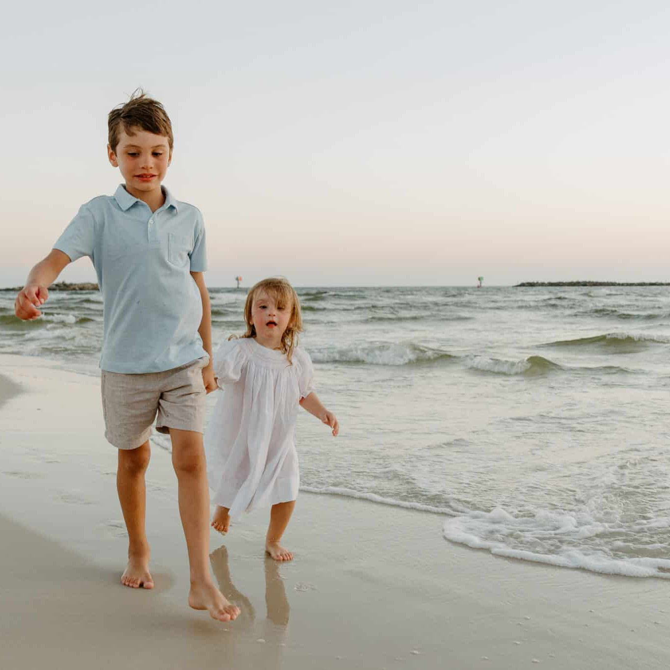 Two young children holding hands and running through the tide on the Florida Gulf Coast.