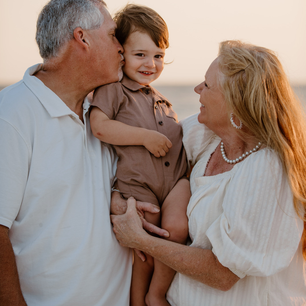 Grandparents hugging their young grandson during a family beach portrait session.
