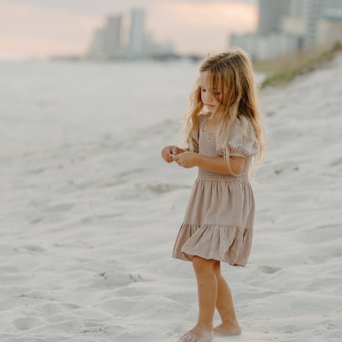 Little girl in a tan dress walking through sea oats on Navarre Beach at sunset. | Close-up portrait of a young girl in a pink dress standing in the sea oats during an Orange Beach photography session.